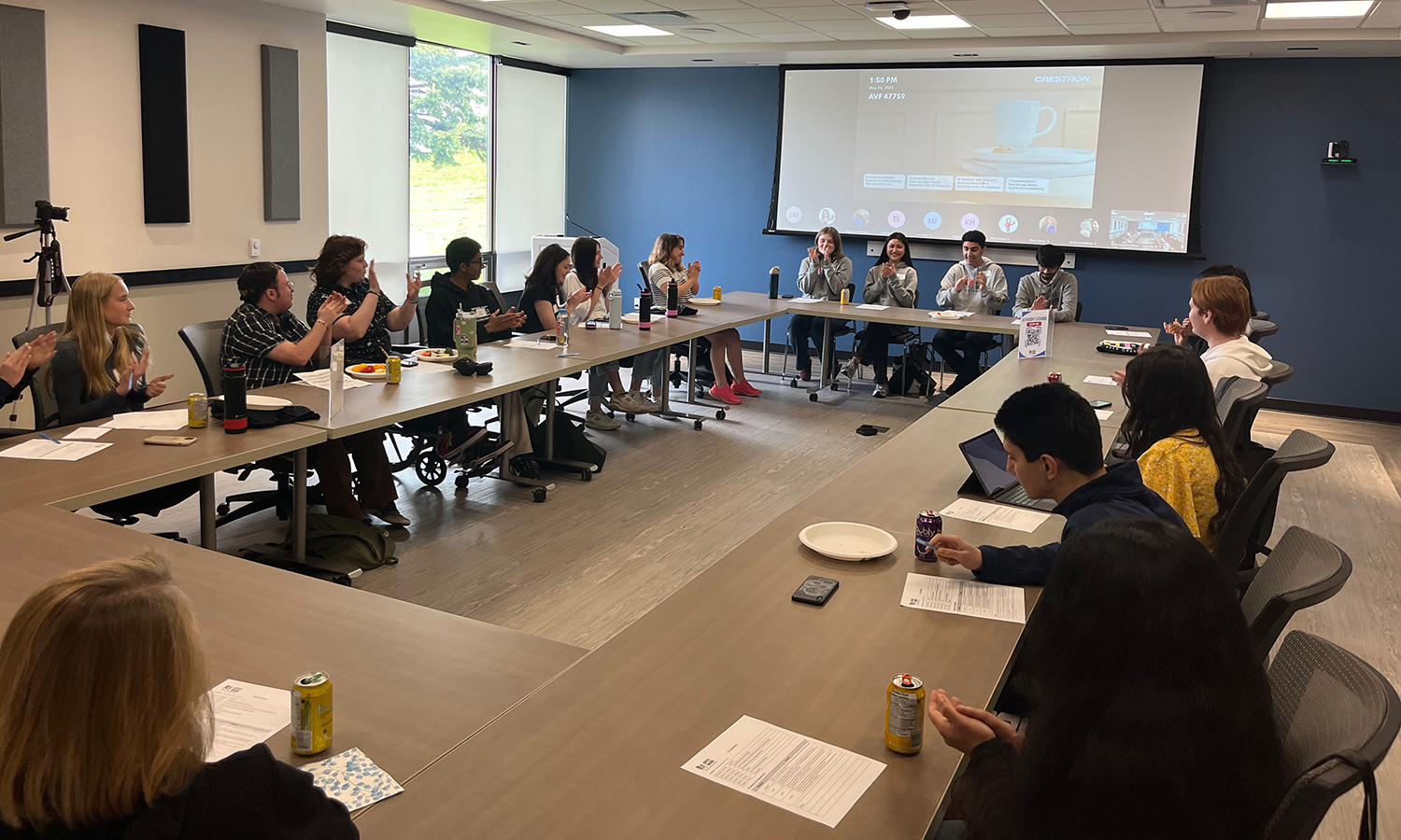 students sit in a meeting room around an oval of tables