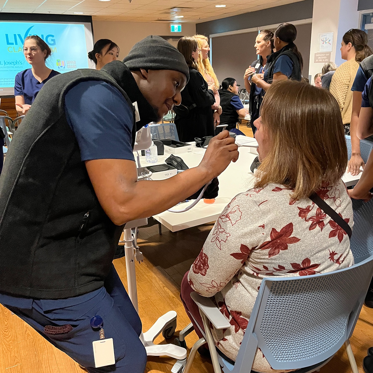 A PSW student takes the temperature of a woman in a chair.