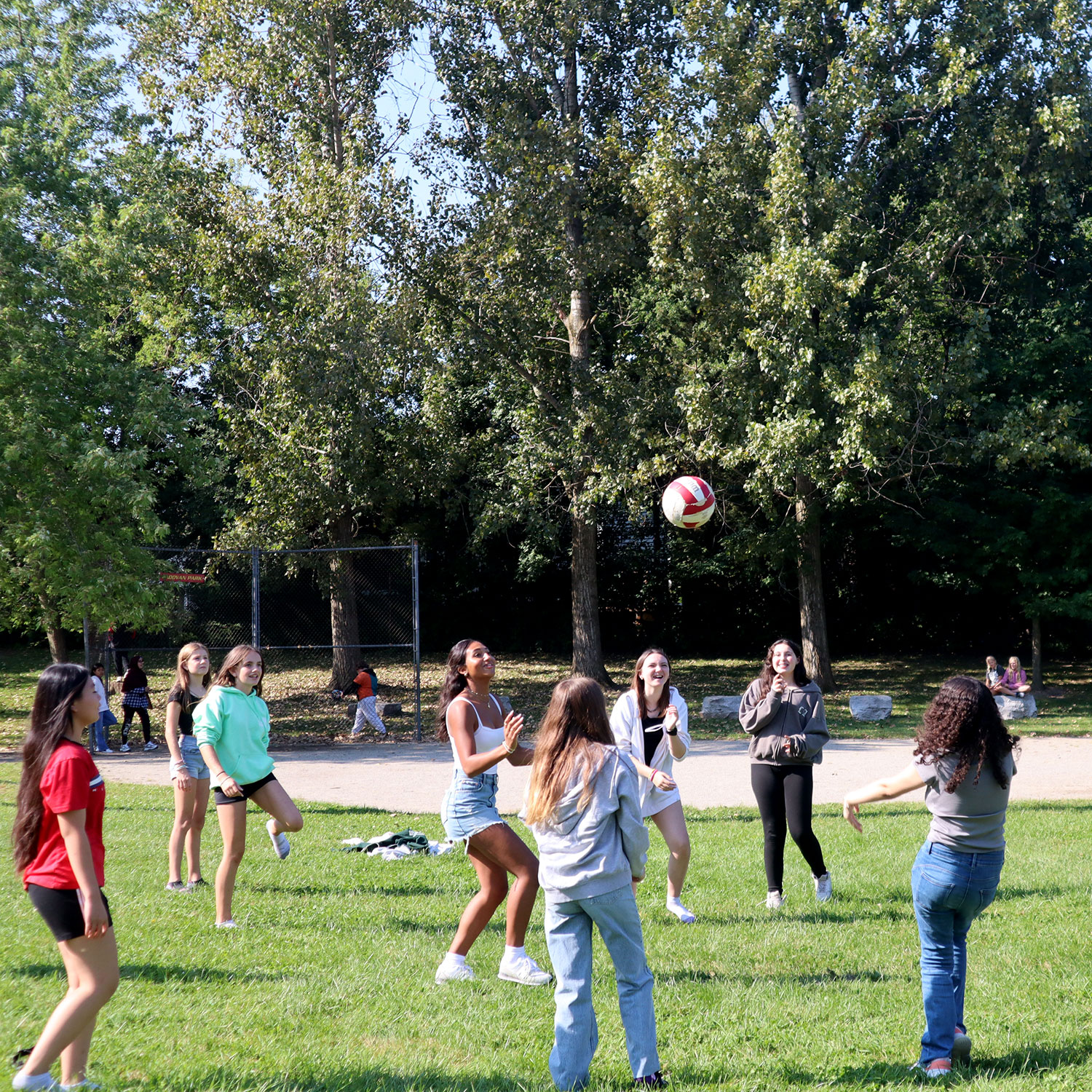 Students play volleyball on grass outdoors.