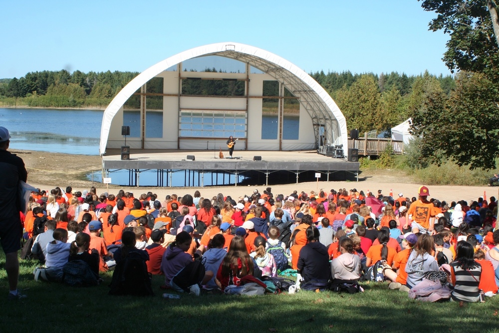 Hundreds of students sit on the grass listening to a musical performance