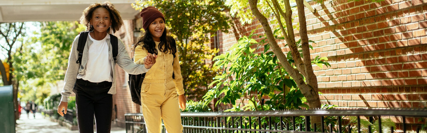 Two youth walk down a sidewalk together, smiling. 