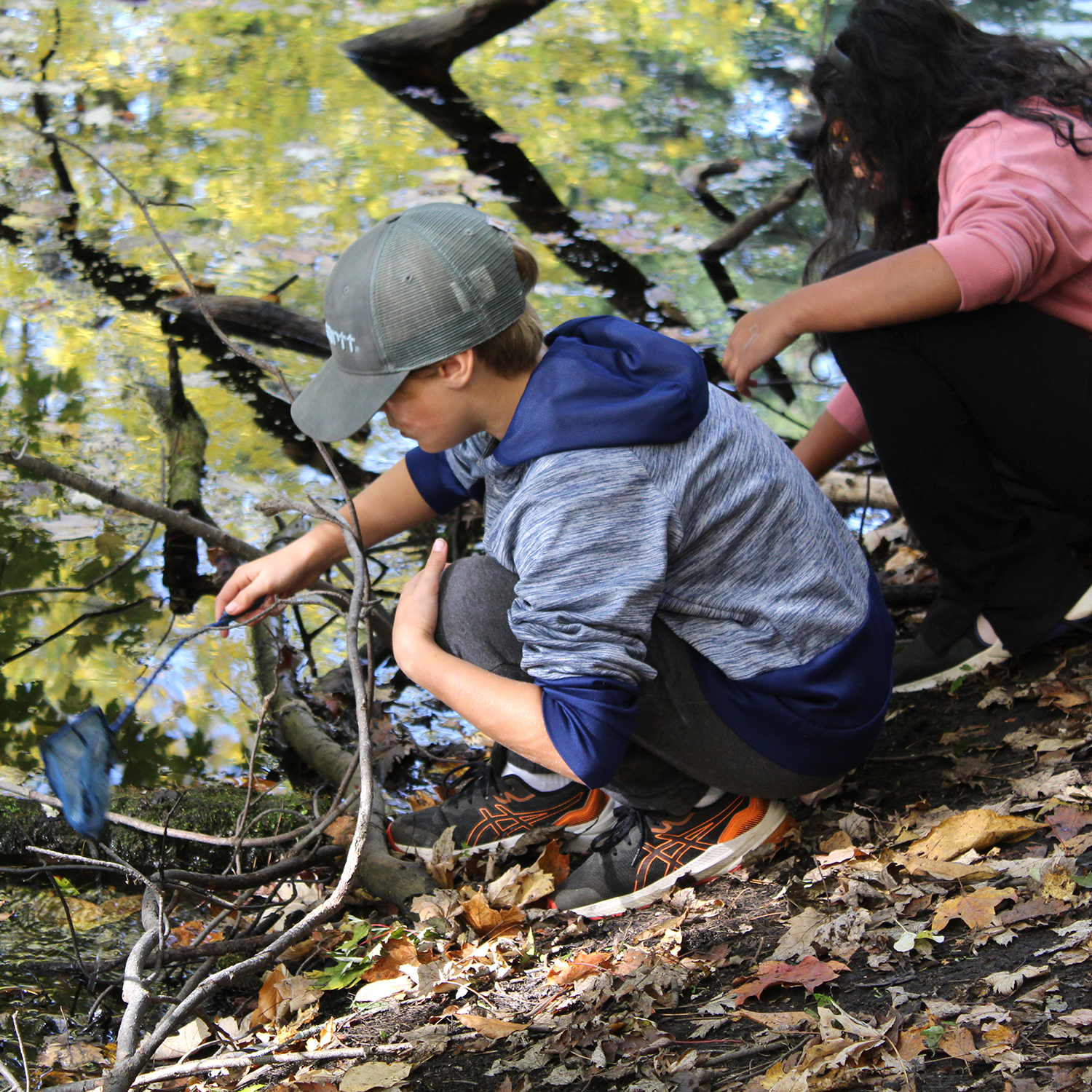 Two students crouch down by a river.