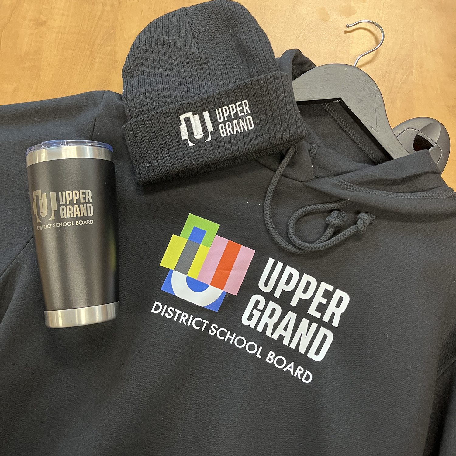 A coffee tumbler, toque and hoodie are pictured with the UGDSB logo on each item.