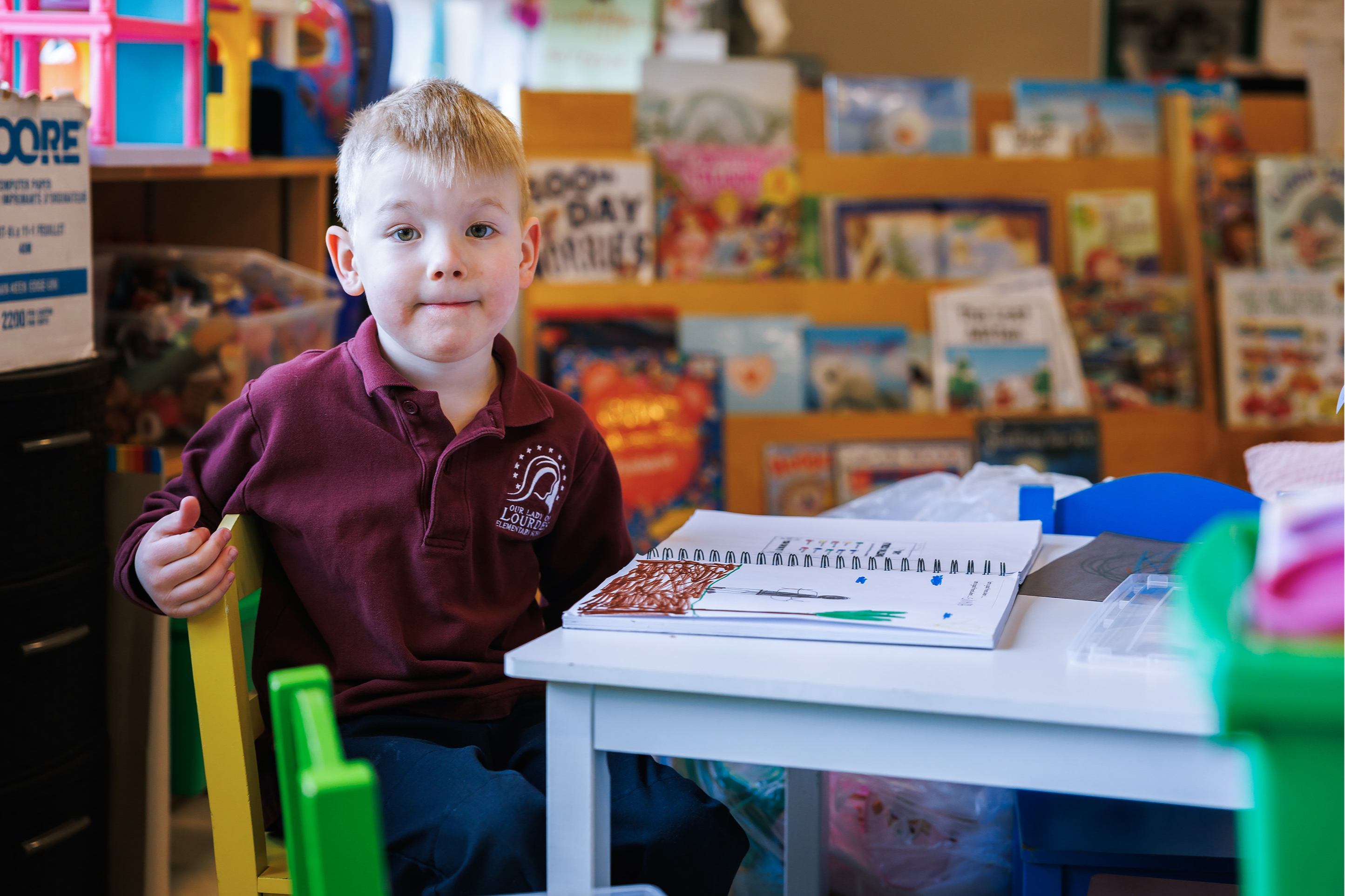 young boy sititng a desk in front of kids books