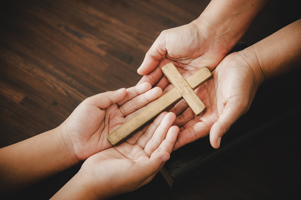 Two sets of hands holding a small wooden cross