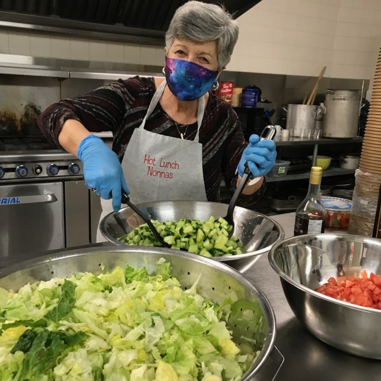 Lady cooking/making a salad with mask and gloves on