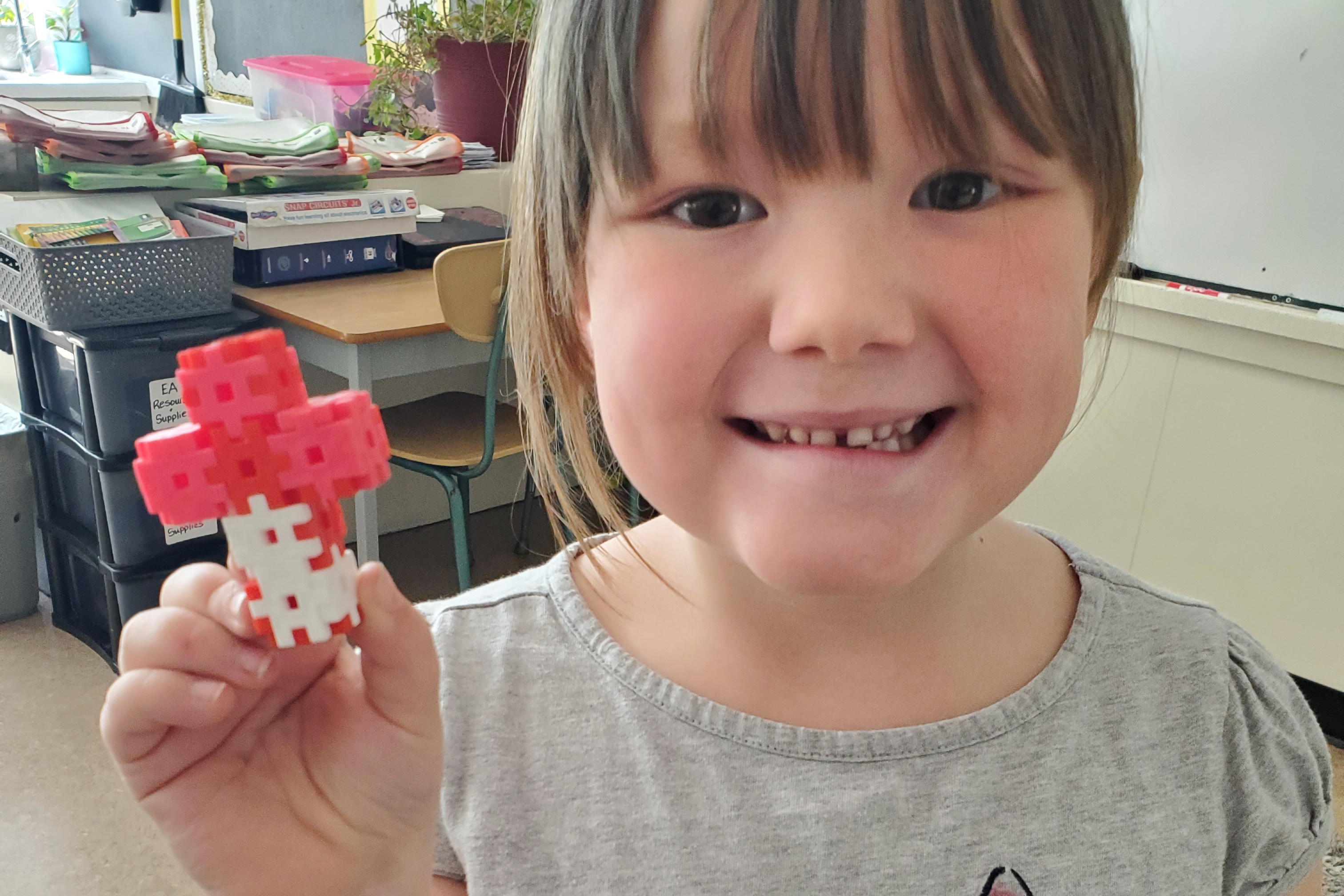 student smiling and holding up a cross made of blocks