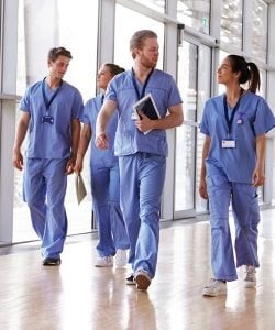 Health care workers in blue scrubs walking together while talking to each other