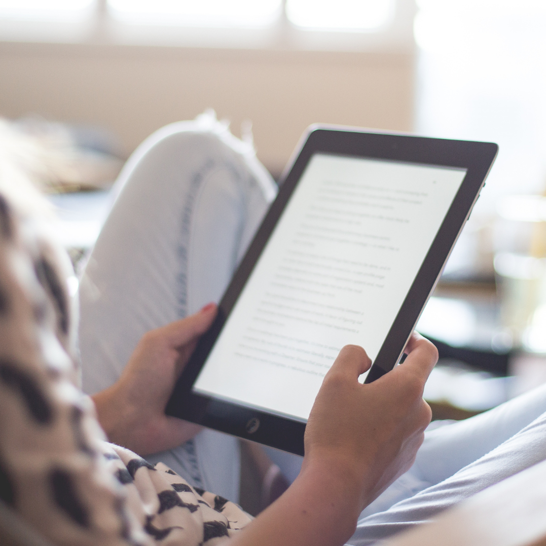 A stck of books with a hand holding a tablet