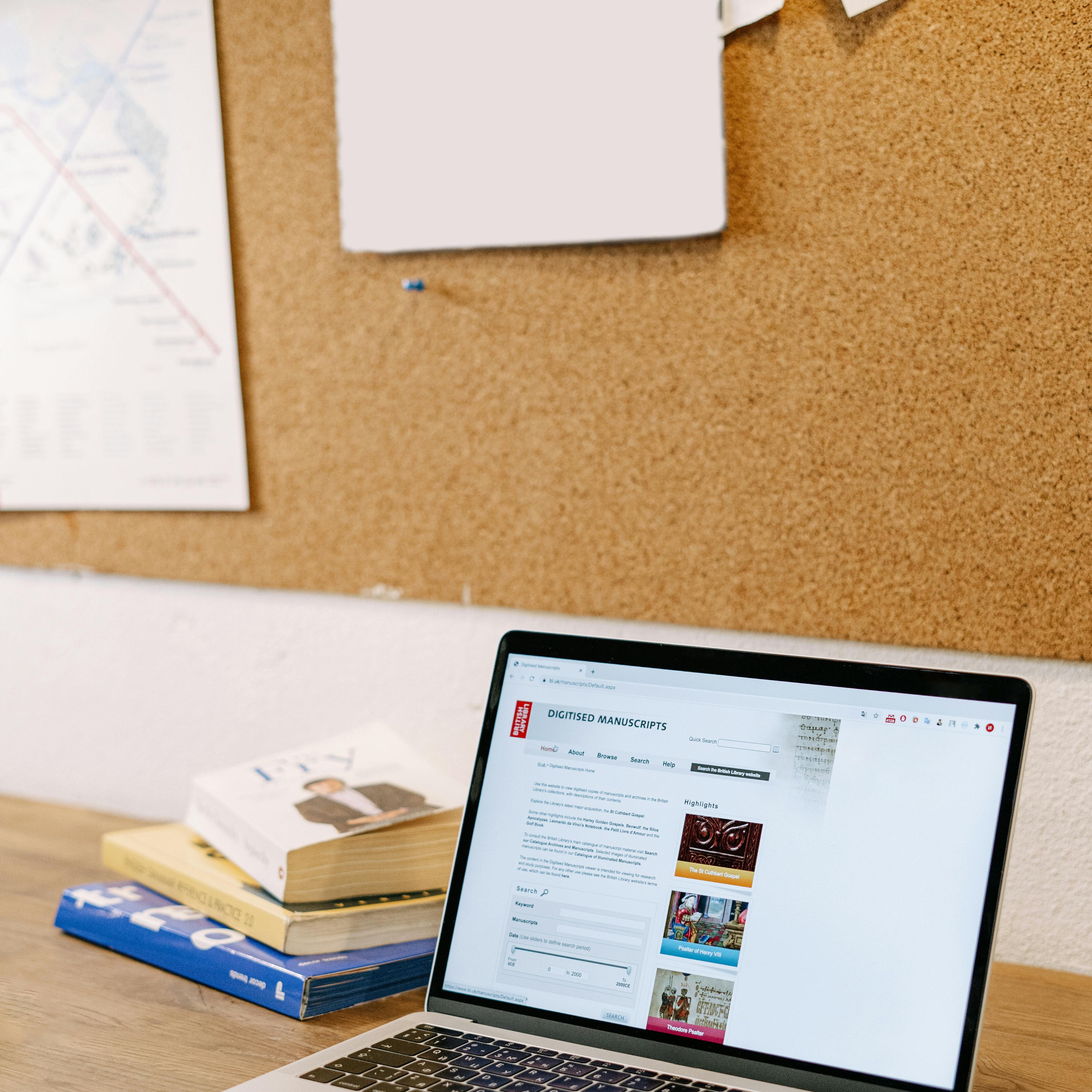 Laptop computer in front of bulletin board beside a stack of books