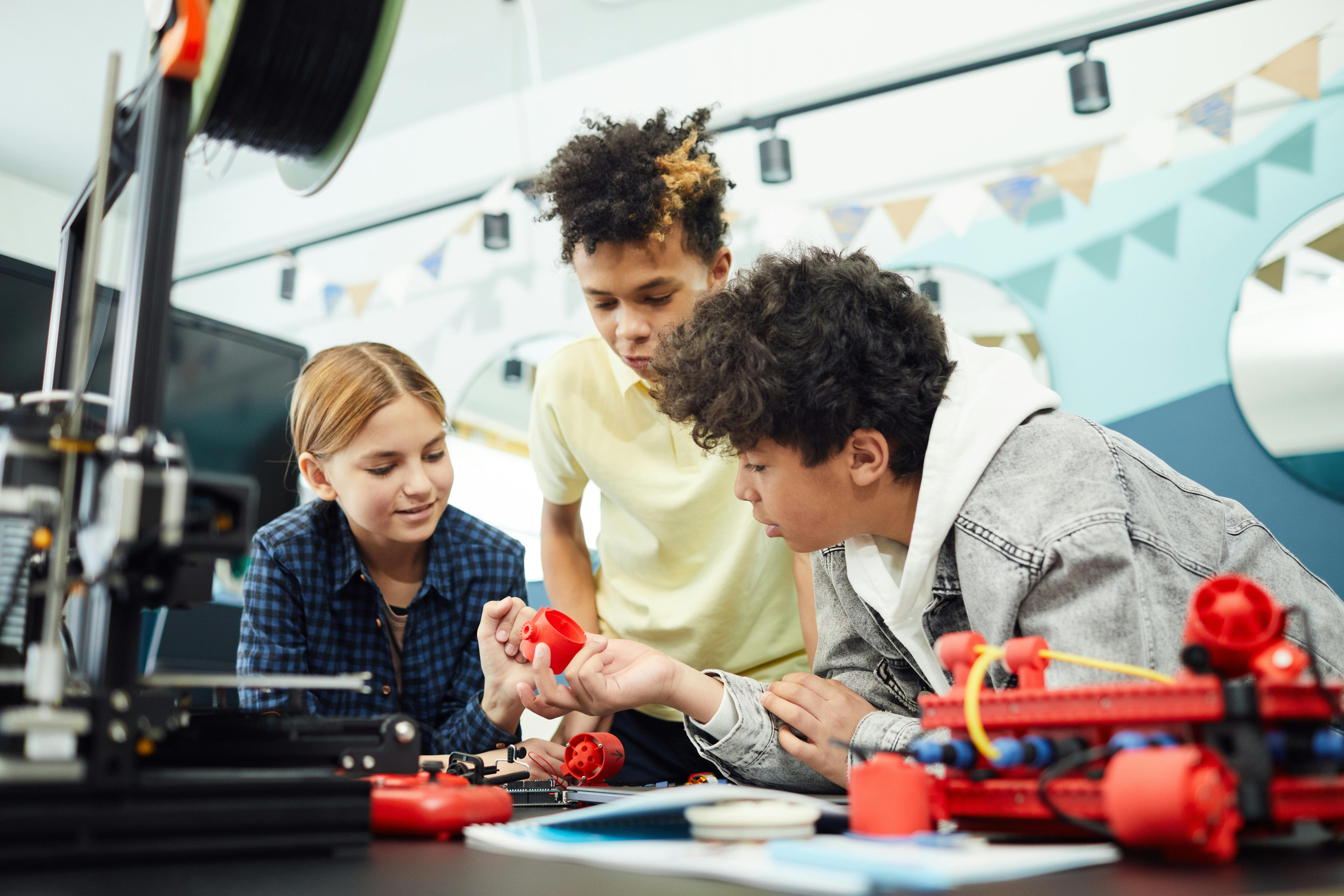 Three students examining 3D printed materials in front of a 3D printer