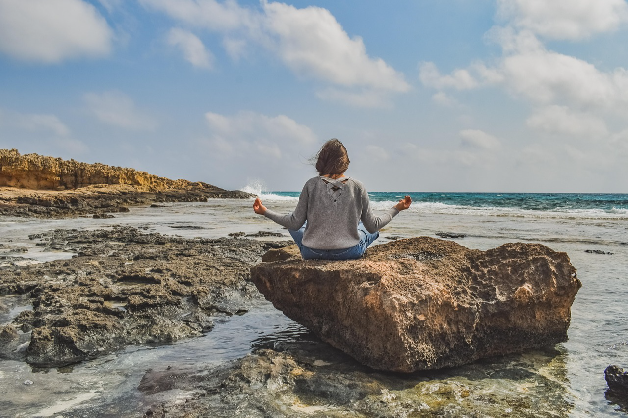 Person sitting on a rock in front of the ocean meditating