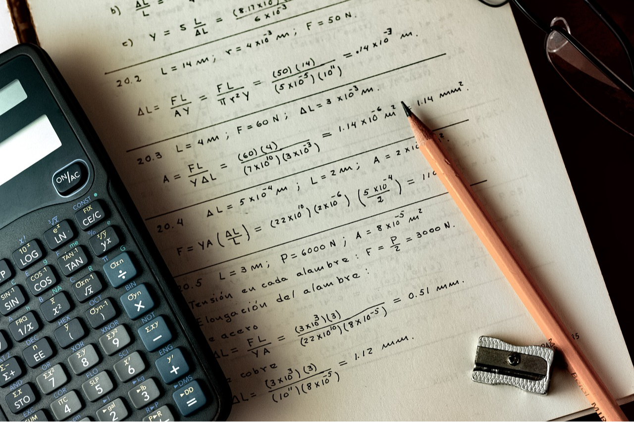 A piece of paper with mathematical equations writen on it and a calculator and pencil