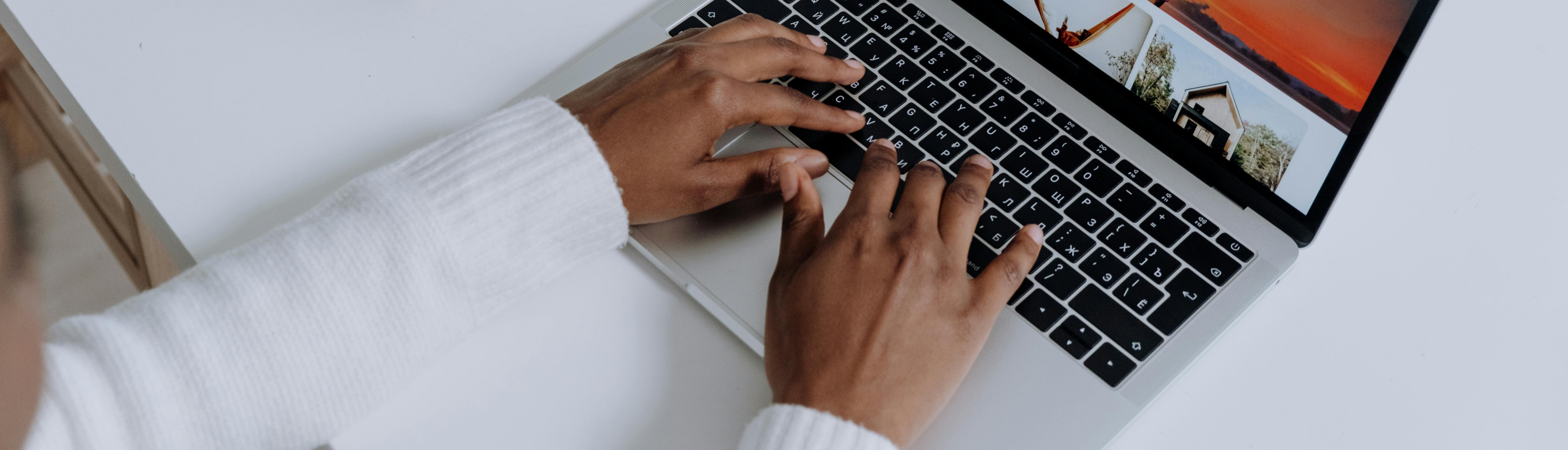 Photo of a person seated at a white table typing on a laptop 
