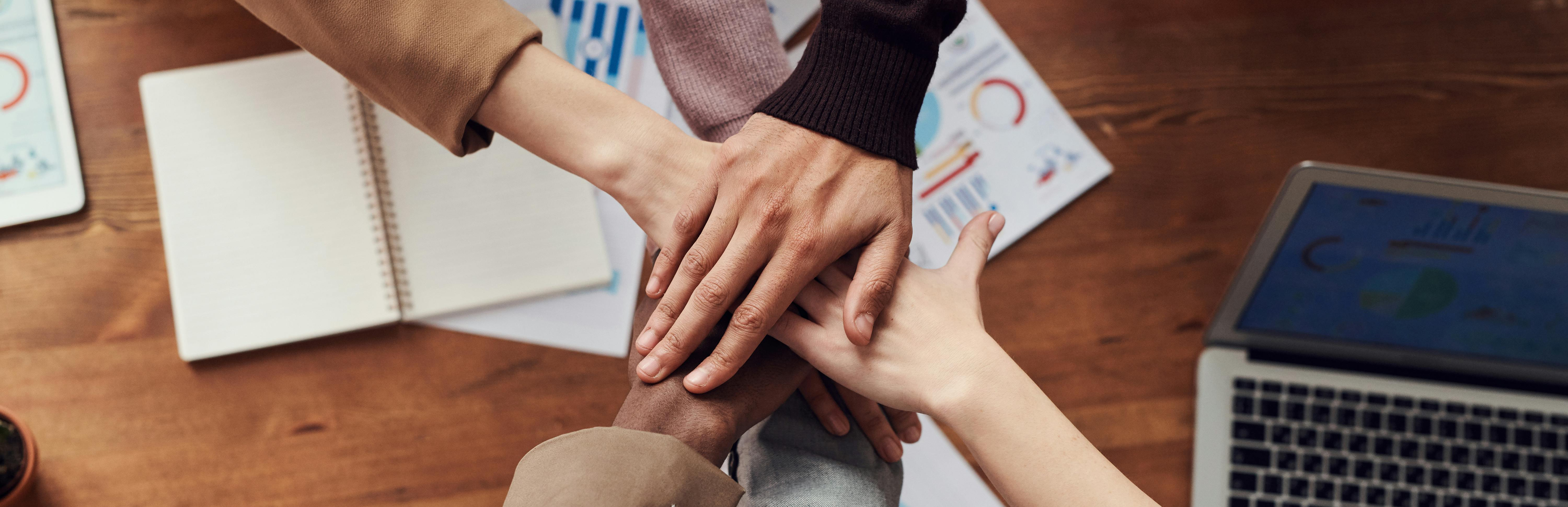 Photo of several people with different skin tones stacking their hands over a desk
