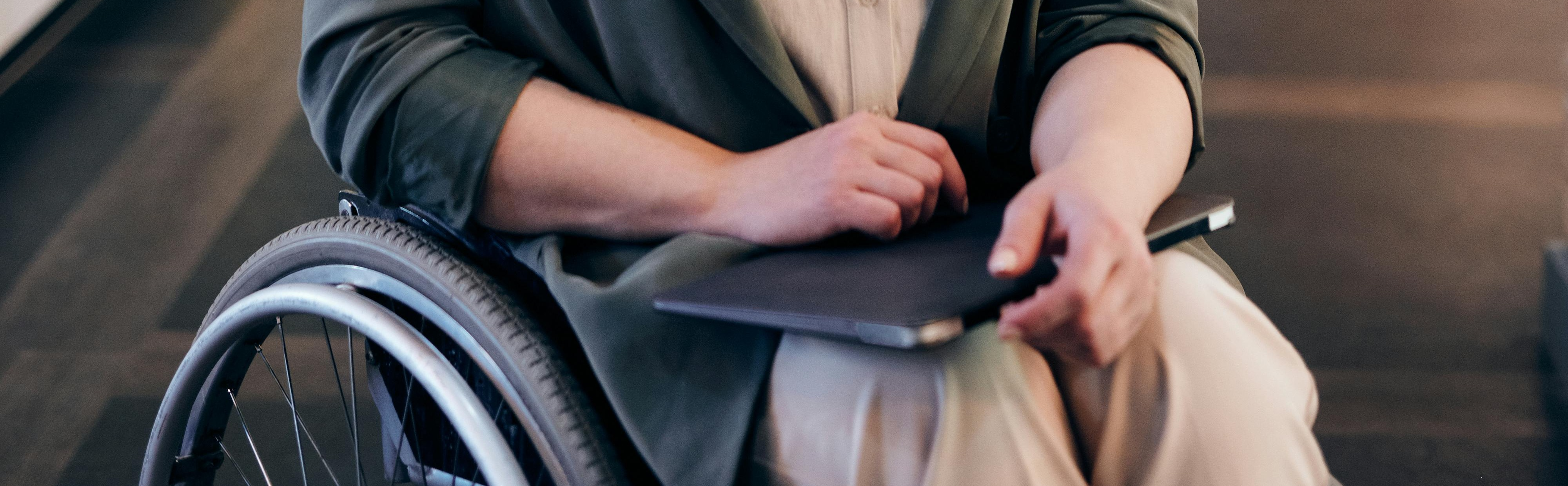 Photo of person sitting in a wheelchair holding a closed laptop on their lap
