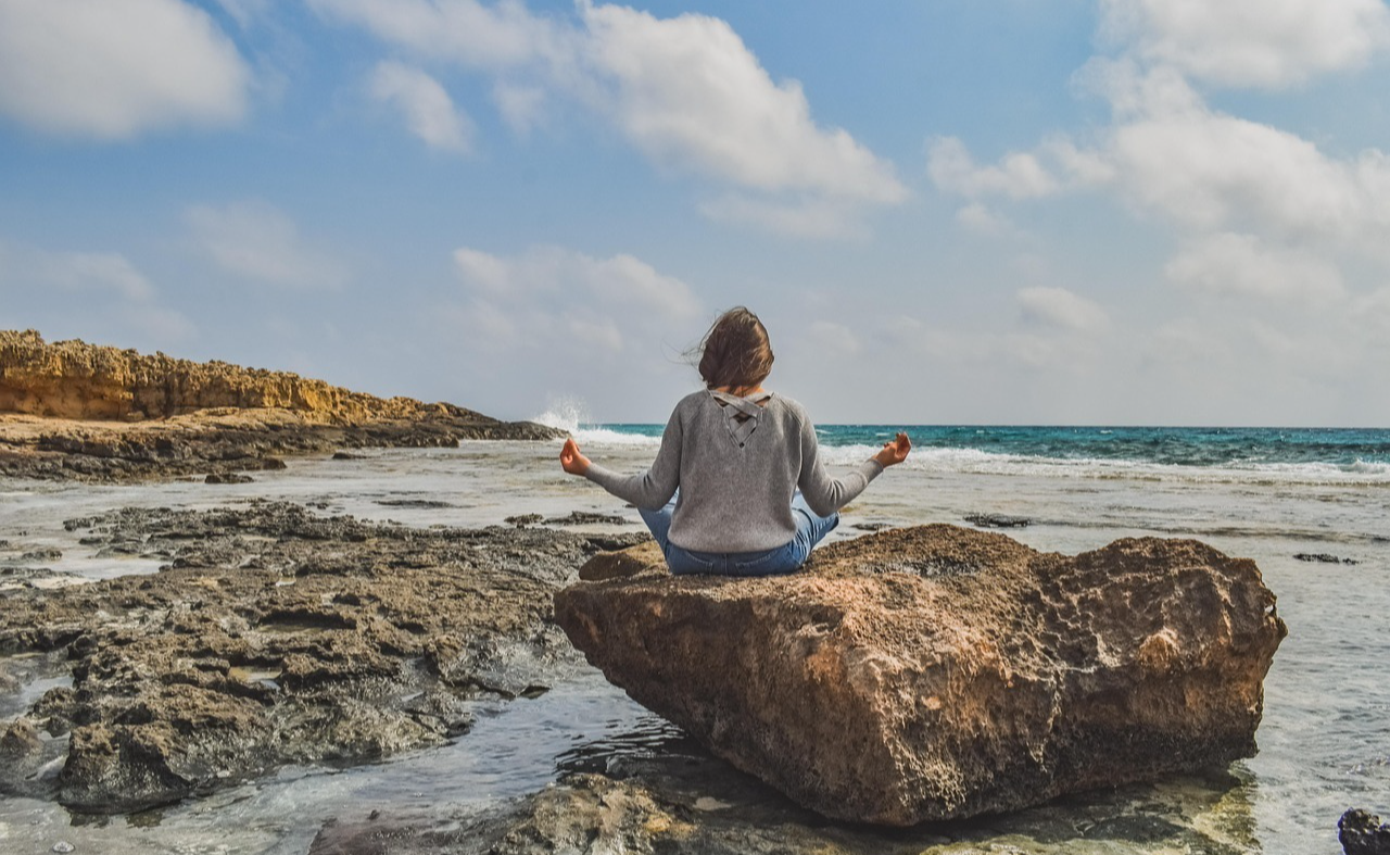 Person sitting on a rock in front of the ocean meditating