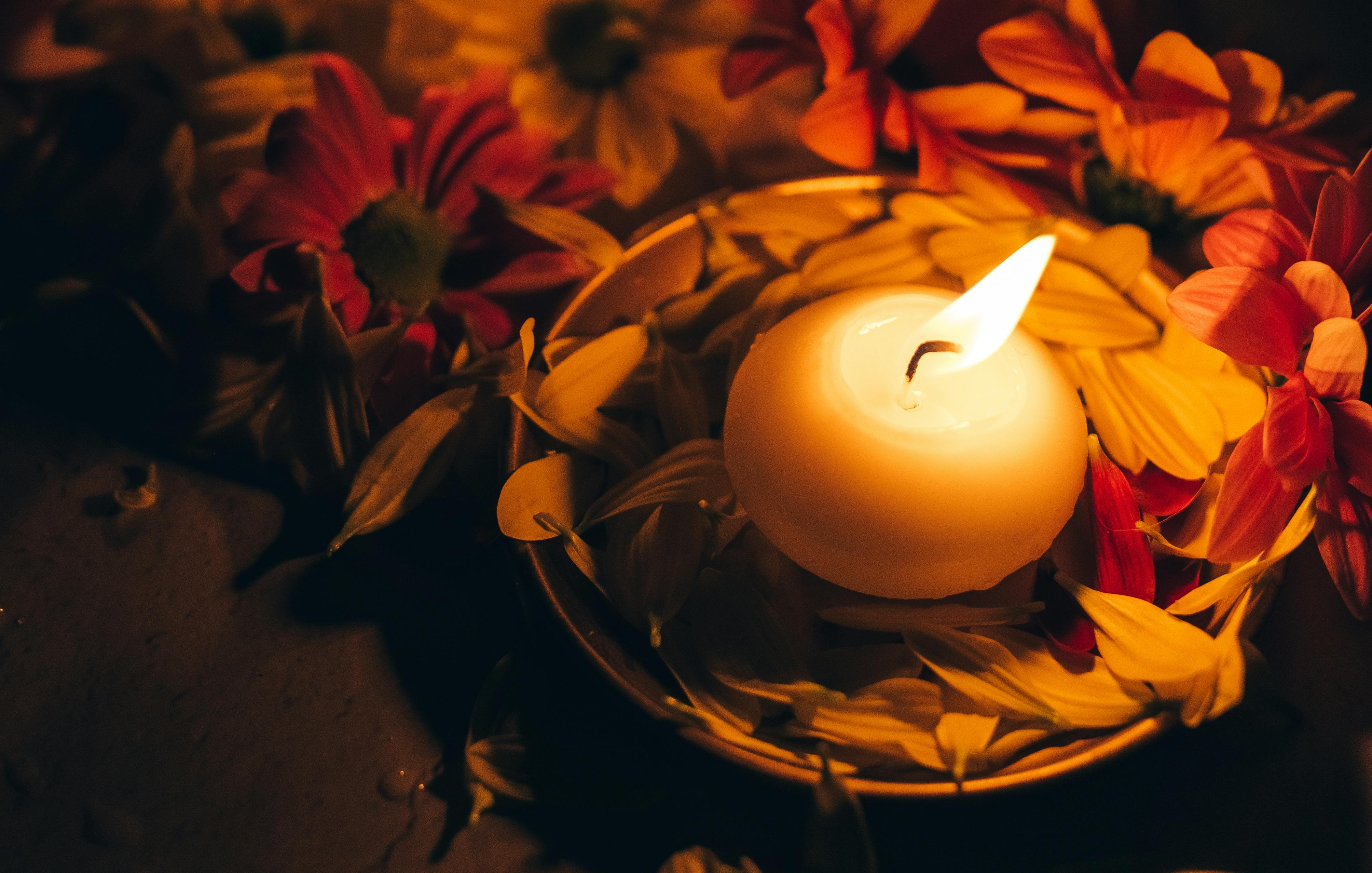 Photo of a small lit candle nestled in a wreath of red and orange flowers