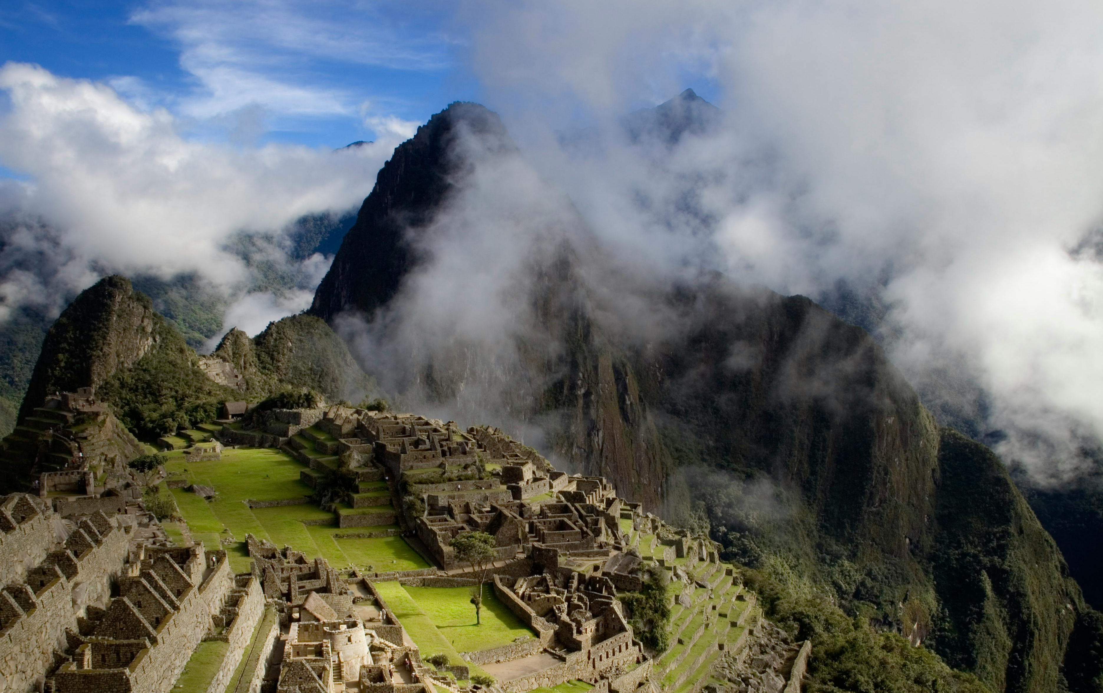 Photo of stone ruins on a grassy mountainside with white clouds and a blue sky